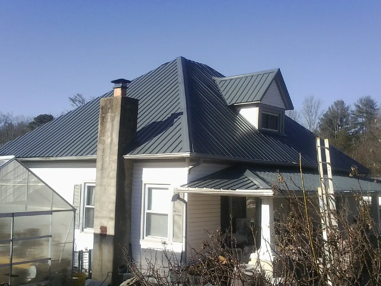 Dark blue standing seam metal roof on a white farmhouse with dormer — Slate & Tile Roof Repair by Roofing Brothers in Mount Upton