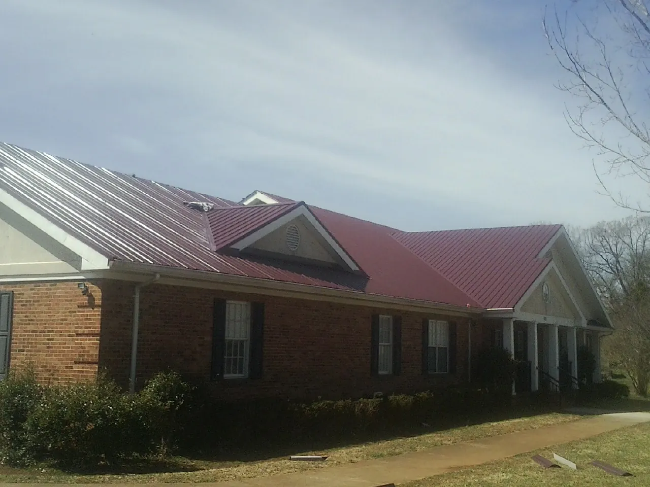 Red metal roof with gabled entries on a long brick building, from a Hail Damage Roof Repair job in Mount Upton