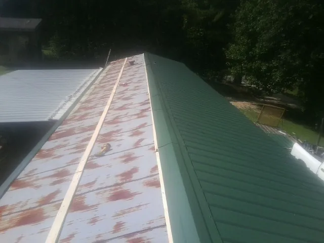 Old rusted panels beside newly installed green metal roofing — Wind Damage Roof Repair by Roofing Brothers in Mount Upton