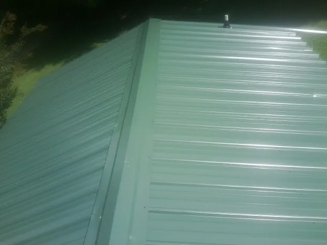 New green metal panels meeting at the ridge of a roof — Flat Roof Repair work by our crew in Mount Upton