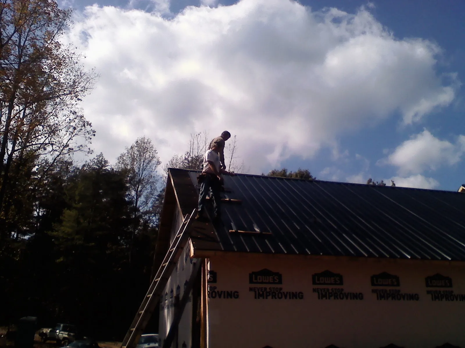 Roofer fastening dark metal panels high against a cloudy sky, from a Roof Inspection job in Mount Upton