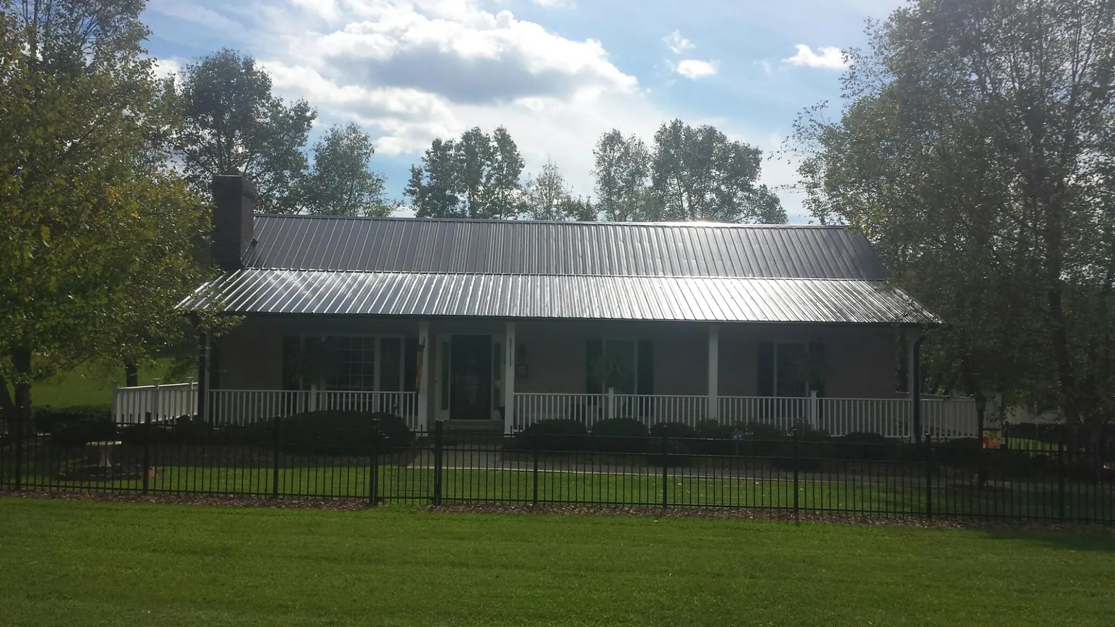 Gray metal roof on a brick ranch with a full width front porch — Gutter Guard Installation work by our crew in Mount Upton