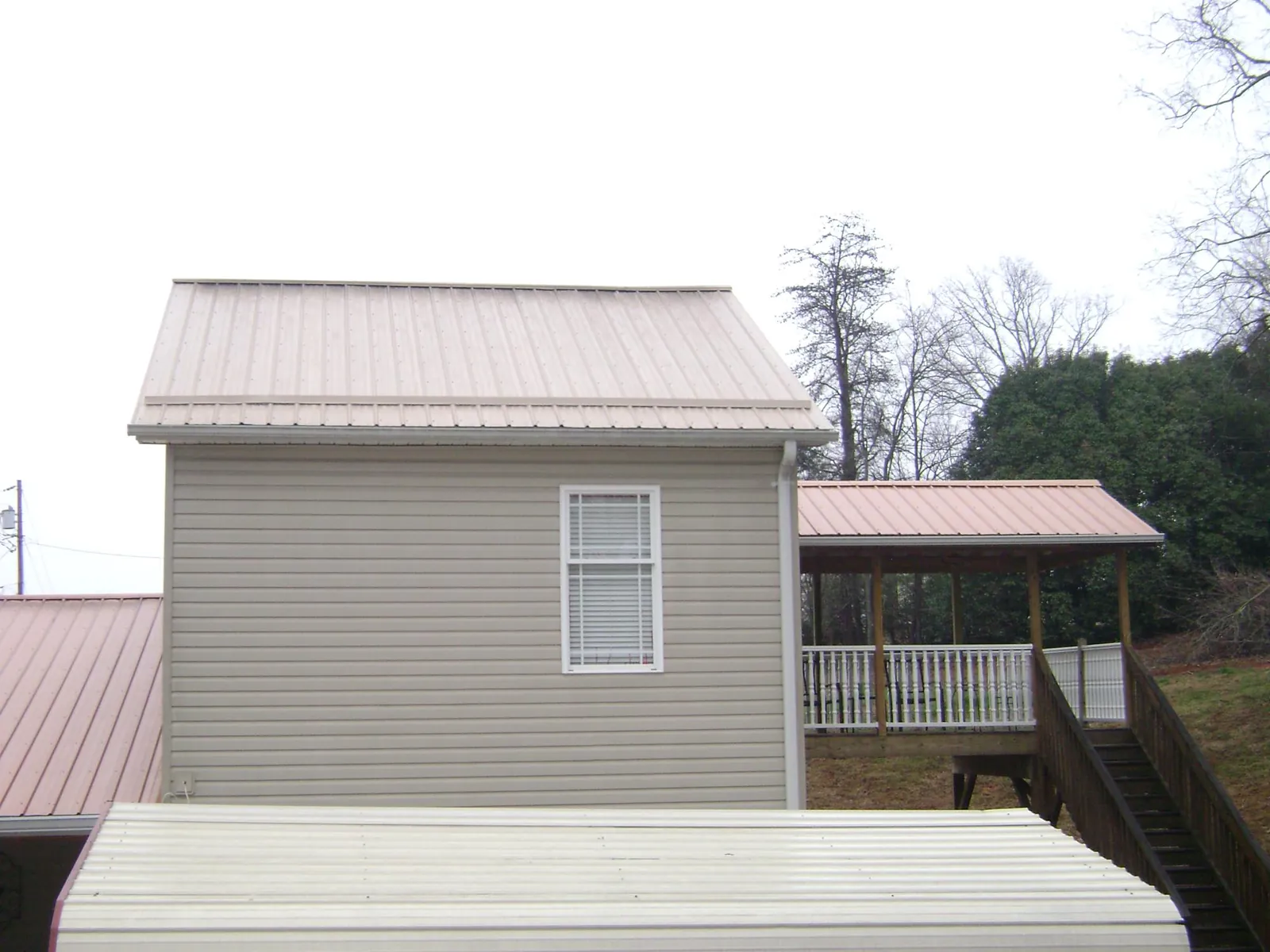 Tan metal roofs on a two story addition and attached porch, from a Roof Replacement job in Mount Upton